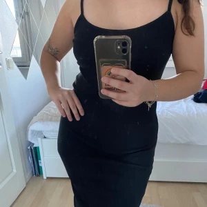 Svart klänning från Amisu - Snygg svart klänning från Amisu med smala axelband och en figurnära passform. Perfekt för en stilren look. Klänningen är ribbad och har en enkel design som gör den lätt att matcha med olika accessoarer.