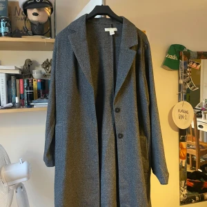Grå trenchcoat från H&M - Säljer en stilren grå trenchcoat från H&M i storlek 42. Den har en klassisk design med knappar framtill och långa ärmar. Perfekt för höst och vår!