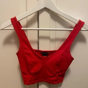 Röd ribbad topp från Monki - Snygg röd ribbad topp från Monki i storlek XS. Toppen har breda axelband och en croppad design som ger en trendig look.