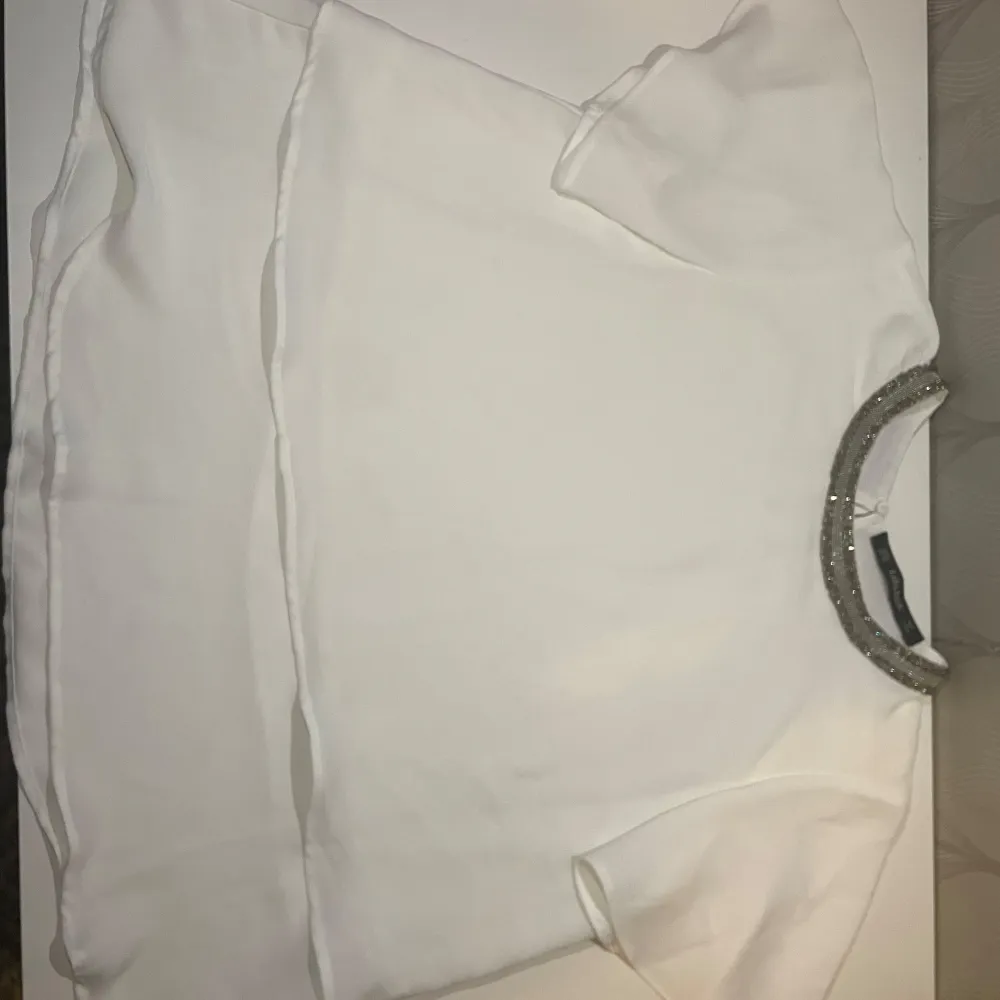 Säljer en stilren vit blus från Zara Basic med korta ärmar och en glittrig detalj runt halsringningen. Perfekt för en elegant look. Den är helt oanvänd utan prislapp. Släjer eftersom den inte kommer till någon användning 💕💕💕. Puserot.