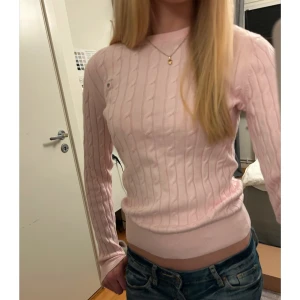 Ljusrosa stickad tröja från GANT - Säljer en ljusrosa stickad tröja från GANT med kabelstickat mönster. Tröjan har långa ärmar och en rund halsringning.🩷