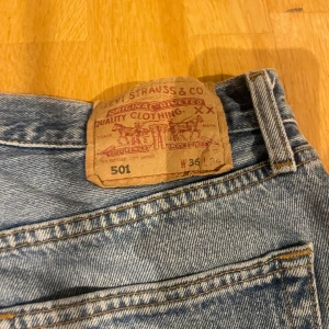 Levi's 501 jeans - Klassiska Levi's 501 jeans i blå denim. Dessa jeans har en rak passform och är tillverkade i slitstarkt bomullsmaterial. De har en knappgylf och fem fickor, vilket ger en tidlös stil. Perfekta för en avslappnad look.