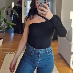 Svart oneshoulder topp från Bubbleroom - Snygg svart oneshoulder topp från Bubbleroom i ribbat material. Perfekt för en stilren look med en unik design. Toppen har en lång ärm och en tight passform som framhäver figuren.