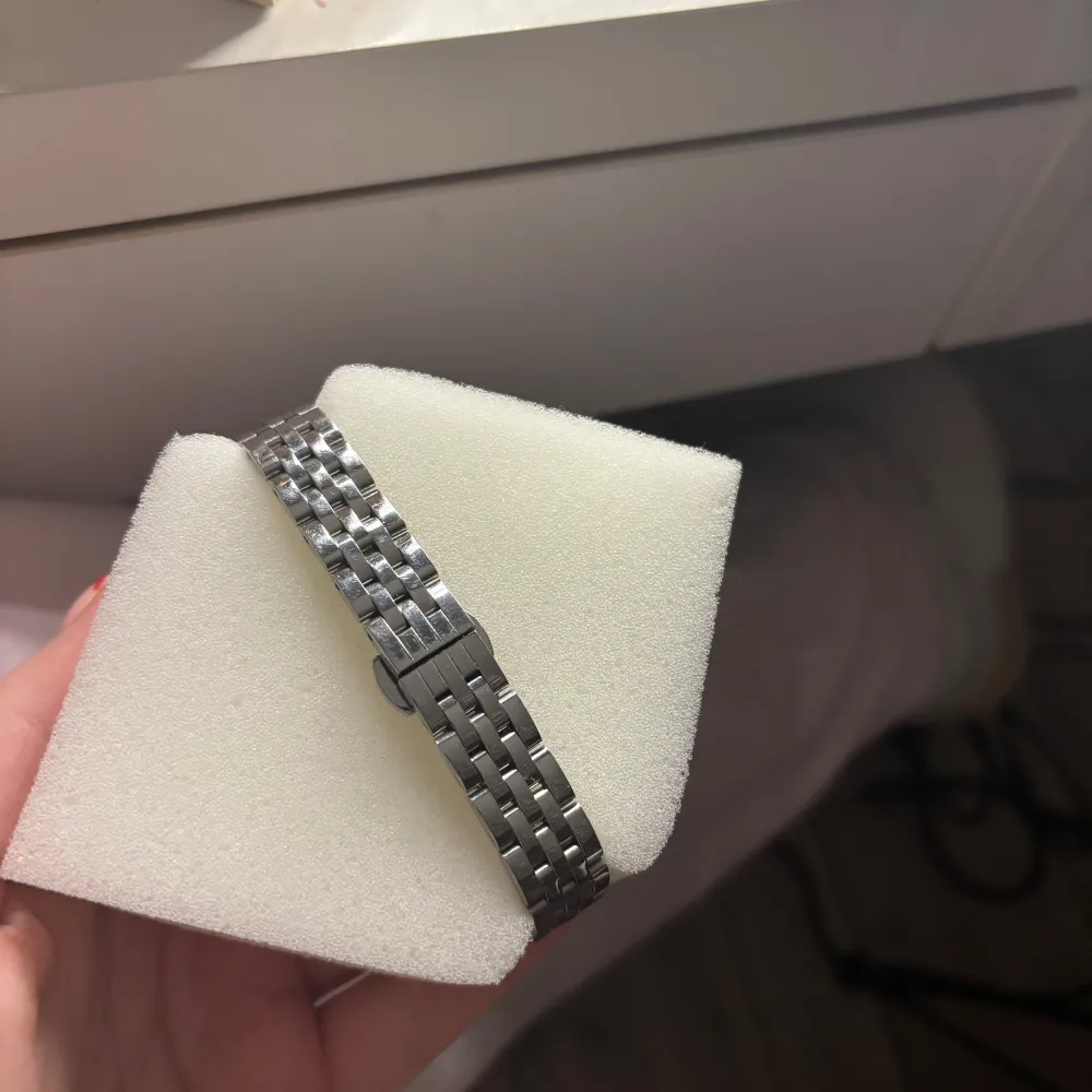 Elegant klocka med rektangulär urtavla och romerska siffror. Den har ett stilrent silverfärgat länkarmband som ger en klassisk look. Typ aldrig använd så den är i superbra skick! Jag har inte tagit bort någon länk så ifall man tycker den är för stor är det inga problem att ta bort . Asusteet.