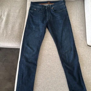 Mörkblå jeans från Hugo Boss - Snygga mörkblå jeans från Hugo Boss med klassisk femficksdesign och orange detaljer. Perfekta för en stilren look. Tillverkade i slitstarkt denim med knappgylf.