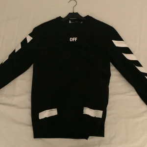 Svart tröja från Off-White - En äkta och snygg svart tröja från Off-White med vita detaljer och ikoniska pilar på ryggen. Texten 'OFF' pryder framsidan och 'SEEING THINGS' finns på baksidan. Perfekt för en trendig look. Säljer för billigt för tagen är borta