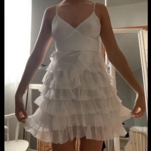 Vit volangklänning med smala axelband - Vit klänning med flera lager av volanger och smala axelband. Klänningen har en omlott-design och knytning i ryggen. Perfekt som en studentklänning 🥰