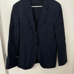 Mörkblå kavaj från Hugo Boss strl 48/M - Snygg mörkblå kavaj från Hugo med klassisk design. Kavajen har två knappar framtill och en stilren passform. Perfekt för både formella och semi-formella tillfällen. Använd två gånger. Mycket bra skick inget slitage, inga märken. Storlek 48/M
