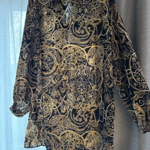 Mönstrad skjortklänning från H&M - Säljer en unik och stilren skjortklänning från H&M med ett detaljerat mönster i guld och svart. Klänningen har långa ärmar och en normal passform, perfekt för att sticka ut i mängden. Ett måste för garderoben!