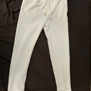 Zara Vita byxor strl M - Säljer ett par bekväma vita byxor från Zara med snörning i midjan. Byxorna har en avslappnad passform och är perfekta för en bekväm stil. De har elastiska muddar vid bensluten för en modern look.                             Inga märken. Inget slitage. Säljes pga att de inte längre passae