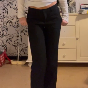 Svarta kostymbyxor - Snygga svarta kostymbyxor med låg midja och bootcut-stil. Perfekta för en stilren look. Byxorna har en klassisk design med dragkedja och knappar framtill.