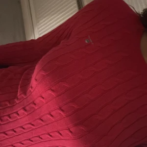 Ceris/röd kabelstickad tröja från Gant - Snygg röd/cerisrosa kabelstickad tröja från Gant med rund hals och långa ärmar. Perfekt för kyligare dagar och ger en klassisk look. Tröjan har en diskret logga på bröstet. Använd någon enstaka gång