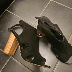 Svarta sandaler med klack - Snygga svarta sandaler i mocka med en stabil träklack. De har en öppen tå och justerbar rem runt ankeln för perfekt passform. Perfekta för en stilren look.