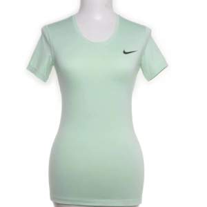 Snygg mintgrön t-shirt från Nike med Dri-FIT-teknologi för optimal komfort och andningsförmåga. Perfekt för träning eller en aktiv vardag. Den har en diskret Nike-logga på bröstet och korta ärmar.