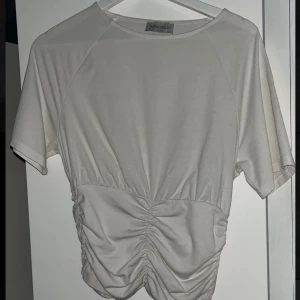 Vit topp från Anna Field - Säljer en stilren vit topp från Anna Field med korta ärmar och rynkade detaljer framtill. Perfekt för en avslappnad look.