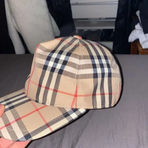 Rutig keps från Burberry - Snygg rutig keps från Burberry i beige, svart och röd. Perfekt för en stilren look med justerbar Storlek. Nästan oanvänd, men inte säker på om den är äkta. 