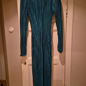 Grön långklänning med randigt mönster - Elegant grön långklänning med ett subtilt randigt mönster. Klänningen har långa ärmar och en smickrande passform som framhäver figuren. Perfekt för speciella tillfällen.