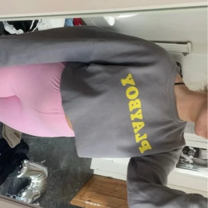 Grå croppad tröja från Playboy - Säljer en supercool grå croppad tröja från Playboy med gult tryck på framsidan. Tröjan har långa ärmar och är perfekt för en avslappnad stil. Den är både bekväm och trendig, perfekt för vardagsbruk! Inga defekter vad jag kan se.