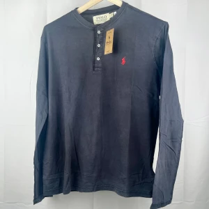 Ralph Lauren - Långärmad tröja - Oanvänd mörkgrå/svart långärmad tröja med vita knappar och broderad logo på bröstet från Ralph Lauren.  Material 100% Bomull 