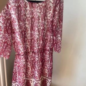 Mönstrad klänning med trekvartsärm - Säljer en superfin klänning med ett rött och vitt mönster. Den har trekvartsärmar och en v-ringad design som ger en snygg look. Perfekt för sommarens fester eller en dag på stan!