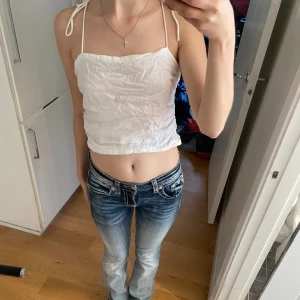 Vit ärmlös linnetopp - Säljer en söt vit linnetopp med tunna axelband som knyts på axlarna. Toppen är croppad och har en avslappnad passform, perfekt för sommardagar. Den är i ett lätt och luftigt material, vilket gör den idealisk för varma väder.