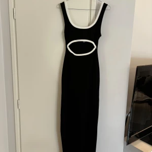 Svart figurnära maxiklänning - Snygg svart tight långklänning från H&M, vita detaljer och cut out framtill, storlek XS, använd 1 gång så som ny 😻🫶🏼 stretchig i tyget. Nypris 299kr