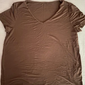 Brun v-ringad t-shirt - Säljer en enkel och stilren brun t-shirt med v-ringning. Perfekt för vardagsbruk och kan lätt matchas med jeans eller shorts. T-shirten har korta ärmar och är gjord i ett mjukt material som känns skönt mot huden.