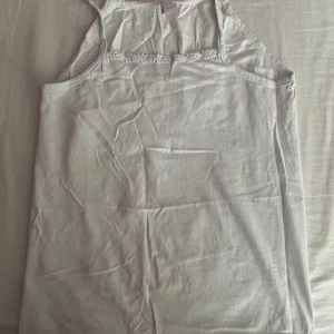 Vit ärmlös linnetopp med spetsdetalj - Säljer en söt vit linnetopp från Yildiz. Den är ärmlös och har en fin spetsdetalj längs halsringningen. Perfekt för sommardagar eller som ett basplagg under en kofta.