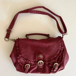 Vin röd väska - Vinröd väska med massa fickor och detaljer. Guldfärgad metall. Småsmå defekter på framsidan (3) Mycket utrymme (4&5). Köp gärna via köp nu, annars går det bra att mötas upp i Stockholm ❤️❤️ 