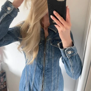 Blå jeansjacka med dragkedja - Snygg blå jeansjacka med dragkedja och knappar på bröstfickorna. Jackan har en figurnära passform och långa ärmar. Perfekt för en cool och avslappnad stil.