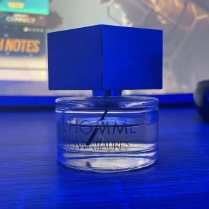 L'Homme Eau de Toilette från Yves Saint Laurent - Elegant och maskulin doft i en stilren flaska med en distinkt blå kvadratisk kork. Perfekt för den moderna mannen som vill utstråla självsäkerhet och stil. Flaskan är genomskinlig och visar den ljusa vätskan inuti. Ungefär 80% kvar