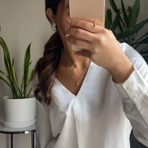 Vit blus från VILA - Elegant vit blus från VILA i storlek 34. Blusen har en v-ringad design och långa ärmar med knappar vid ärmsluten. Perfekt för en stilren look.