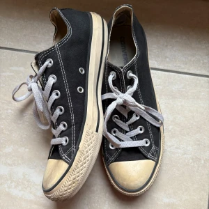 Svarta låga Converse - Säljer ett par klassiska svarta Converse sneakers med vita snören och gummisula, storlek 7. Perfekta för en avslappnad stil. ——————— relativt välanvända, slitage i hälen och missfärgning i gummit.