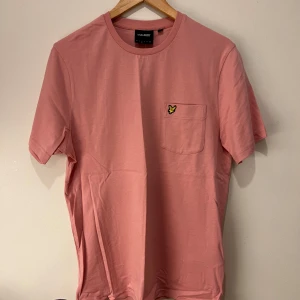 Rosa t-shirt från Lyle & Scott - Säljer en snygg rosa t-shirt från Lyle & Scott med en liten bröstficka och deras ikoniska logga i gult.  Denna tröja är använd 1 gång och passar inte längre där av varför den säljs, priset är relativt billigt p.g.a priset. Om du har fler frågor så är det bara att fråga i dm!