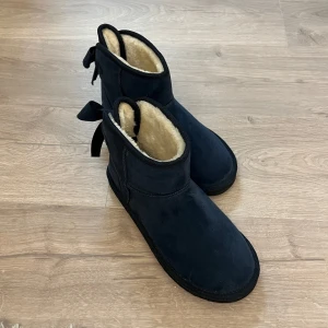 Marinblå boots med rosett - Säljer ett par marinblå boots med mysigt foder och dekorativa rosetter baktill. Perfekta för kyliga dagar. De har en enkel och stilren design som passar till många olika outfits. Liknar Uggs🤍 Säljes pga att de inte kommit till användning! 