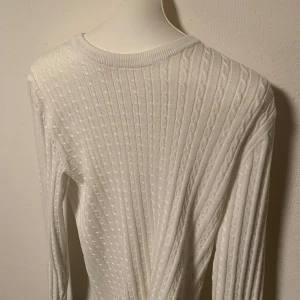 Vit stickad tröja från Jack & Jones - Säljer en stilren vit stickad tröja med ett diskret kabelmönster. Tröjan har långa ärmar och en rund halsringning, perfekt för kyligare dagar. Passar bra till både jeans och kjol. Storlek S