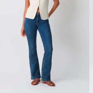 Blå bootcut jeans - Snygga blå bootcut jeans med klassisk femficksdesign och knappgylf. Perfekta för en avslappnad stil med en touch av retro. Passar bra med både sneakers och klackar. Det är även low waist och i strl 40 aldrig använda och prisladden kvar, säljer pga fel storlek, orginal pris 500kr