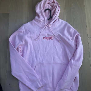 Rosa hoodie från Clean - Säljer en ljusrosa hoodie från Clean med tryck framtill. Den har en klassisk känguruficka och justerbar huva med dragsko. Perfekt för en avslappnad stil. 💖