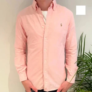 Rosa skjorta från Ralph Lauren - Snygg rosa skjorta från Ralph Lauren med klassisk krage och knappar framtill. Den har långa ärmar och en liten broderad logotyp på bröstet. Perfekt för en stilren look.