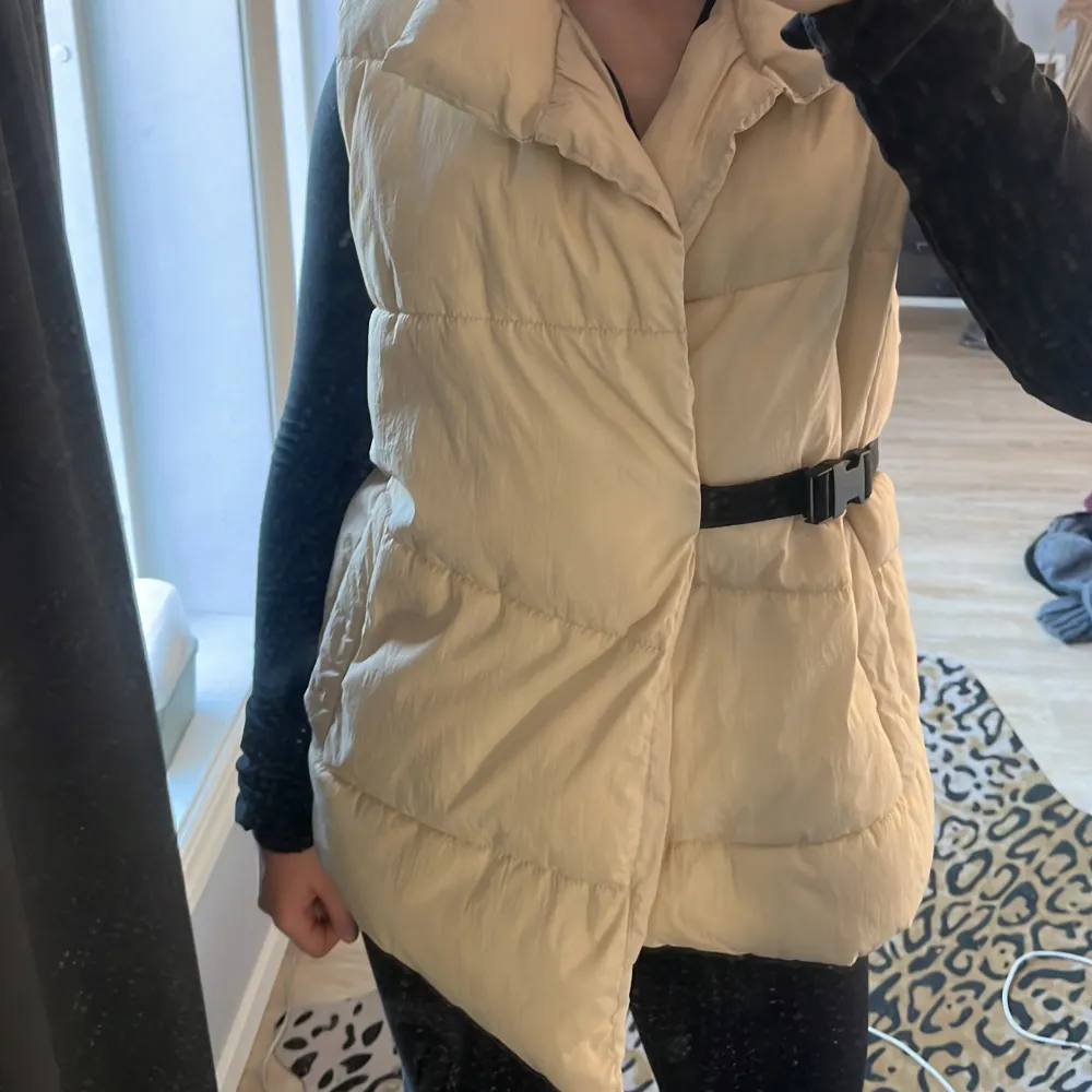 Säljer en snygg beige dunväst från Zara med ett praktiskt bälte i midjan. Jag är 160 cm , Västen har en hög krage och är perfekt för kyligare dagar. Den är quiltad och ger en stilren look.. Takit.