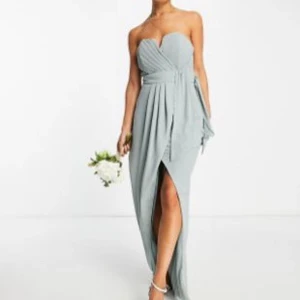 Salivgrön/mintgrön långklänning - Mintgrön långklänning med omlott-design och bandeau upptill. Klänningen har en smickrande passform med veckade detaljer i midjan som ger en fin siluett. Perfekt för bröllop, bal och andra festliga tillfällen. Använd en gång, som ny! Köpt från asos