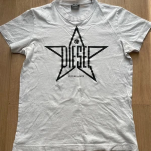 Vit t-shirt från Diesel med stjärntryck - Säljer en vit t-shirt från Diesel med ett coolt svart stjärntryck och texten 'FUTURE is NOW'. Perfekt för en avslappnad stil. T-shirten har en klassisk passform och är kortärmad. Storlek S