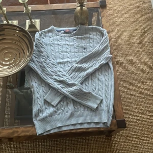 Grå kabelstickad tröja från Morris - Säljer en stilren grå kabelstickad tröja från Morris i 100% Pima Cotton. Tröjan har en klassisk rund hals och långa ärmar, perfekt för kyligare dagar. Den mjuka bomullskvaliteten gör den både bekväm och hållbar.