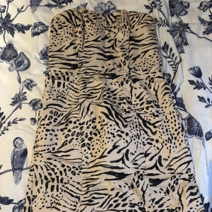 Axelbandslös klänning med djurmönster - Snygg axelbandslös klänning med ett djärvt djurmönster i beige och svart. Perfekt för att sticka ut med sin unika design. 