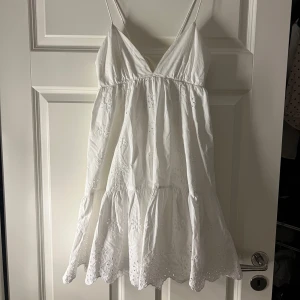 Vit studentklänning med broderade detaljer - Vit klänning med smala axelband och v-ringning. Klänningen har broderade detaljer och en knytning i ryggen. Perfekt för varma studenten. Storlek M men passar S/M. Endast använd fåtalet gånger.