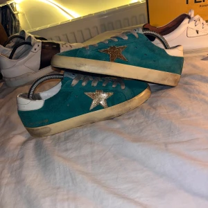 Turkosa sneakers från Golden Goose - Snygga turkosa sneakers från Golden Goose med glittrig stjärndetalj på sidan. Skorna har vita detaljer och en robust sula. Perfekta för en trendig look med en touch av glitter.