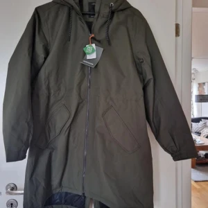 Olivgrön parkajacka med huva - Snygg olivgrön parkajacka med huva och dragkedja framtill. Jackan har långa ärmar och praktiska fickor på sidorna. Perfekt för kyligare dagar och ger en stilren look.