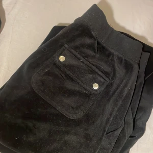 Svarta byxor från Juicy Couture - Snygga svarta byxor från Juicy Couture i mjukt material. Byxorna har en praktisk ficka med knappar och en bekväm passform. Perfekta för en avslappnad stil.