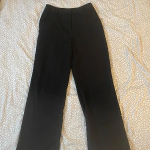 Svarta kostymbyxor från BikBok - Snygga svarta kostymbyxor från BikBok i storlek 38. De har en klassisk design med rak passform och hög midja, perfekta för en stilren look. Byxorna är tillverkade i ett bekvämt material som ger en elegant känsla.