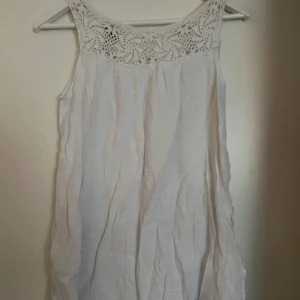 Vit ärmlös klänning med spetsdetaljer från Soaked in Luxury - Säljer en söt vit klänning med spetsdetaljer upptill. Klänningen är ärmlös och har en luftig passform, perfekt för varma dagar. Den är gjord i ett lätt material som ger en skön känsla. Passar bra till sommarens alla tillfällen.
